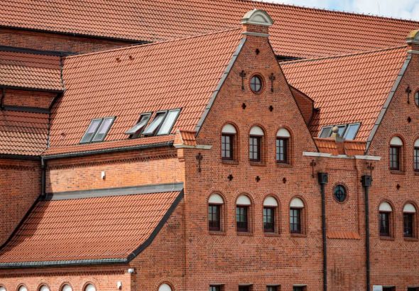 Red brick facade of a historic building in Gdańsk, Poland with intricate roof design.