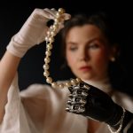 A woman with a prosthetic hand gracefully holding a pearl necklace, showcasing elegance and modern technology.